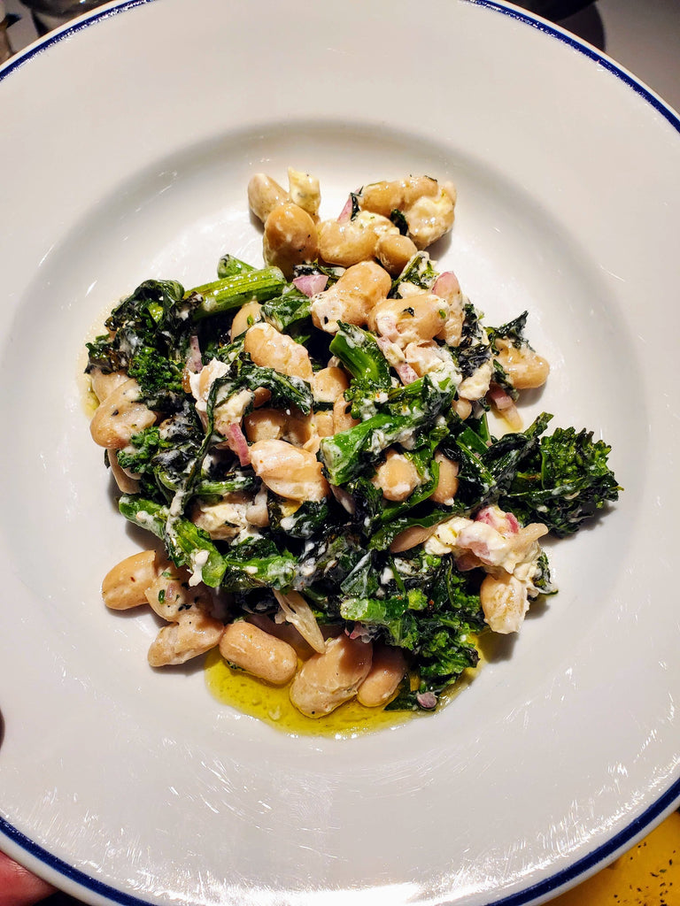 White bean and grilled broccoli rabe on white plate with olive oil drizzle