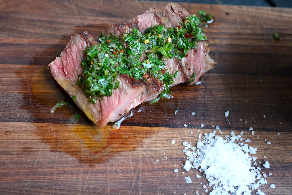 Sliced steak with chimichurri sauce and salt on a wooden cutting board