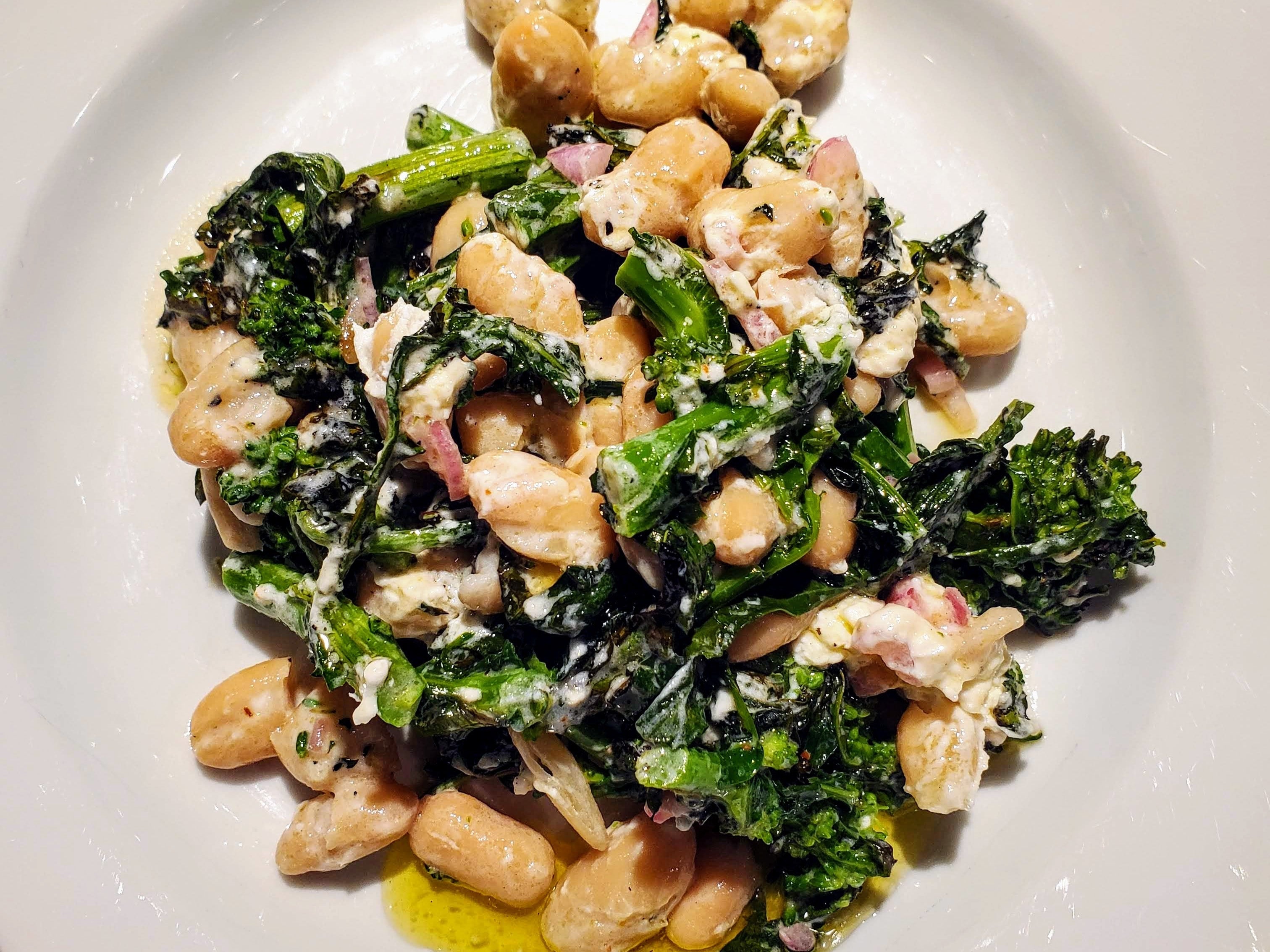 White bean and grilled broccoli rabe on white plate with olive oil drizzle