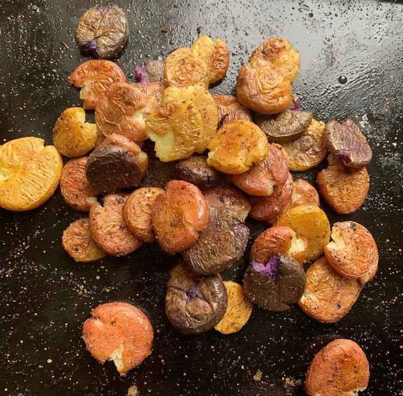 Roasted curry baby potatoes halved and golden-brown with purple & yellow skins on dark baking sheet
