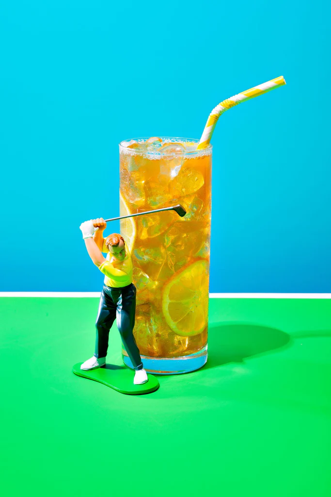 Iced Arnold Palmer in tall glass with lemon and straw on green surface with a miniature golfer