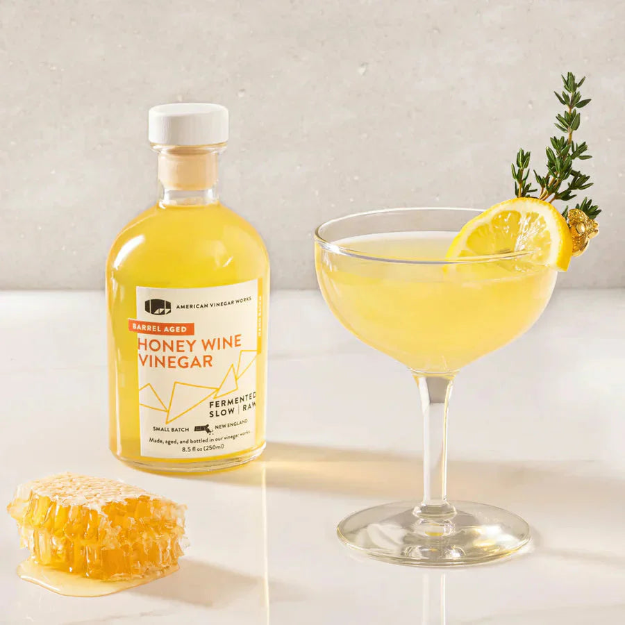 Bee’s Knees cocktail by Honey Wine Vinegar bottle and honeycomb on a light marble surface piece