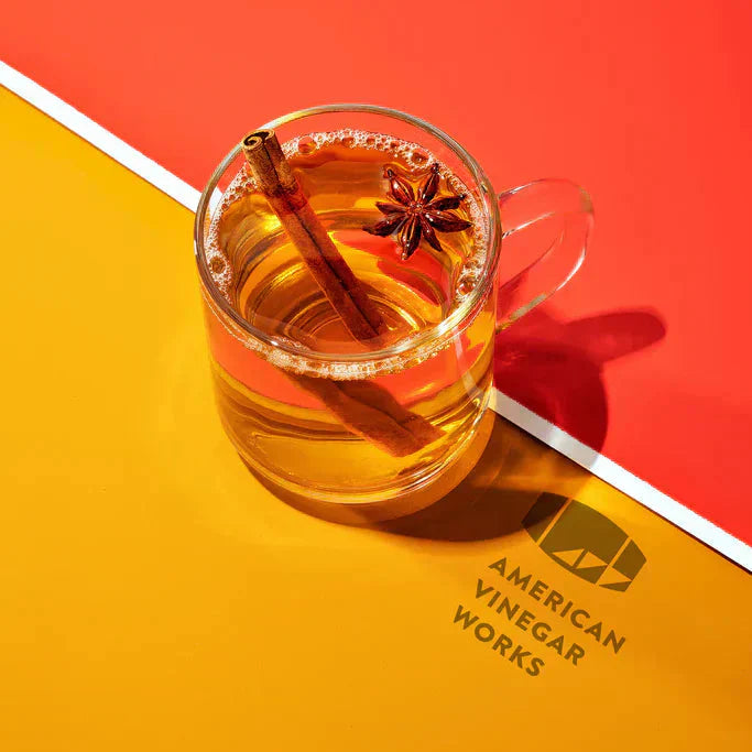 Top-down of hot apple cider in glass mug with cinnamon and star anise on red-and-yellow background