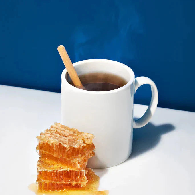 Steaming mug of cider vinegar hot toddy with wooden stirrer and dripping honeycomb on white surface