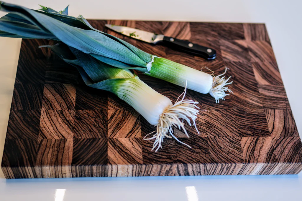 Two whole leeks on a patterned wooden cutting board with a paring knife in the background