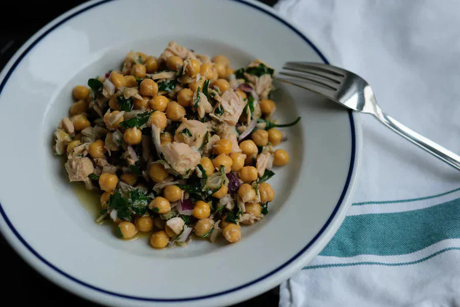 Top-down view of chickpea and tuna salad with red onion and parsley on a white rimmed plate