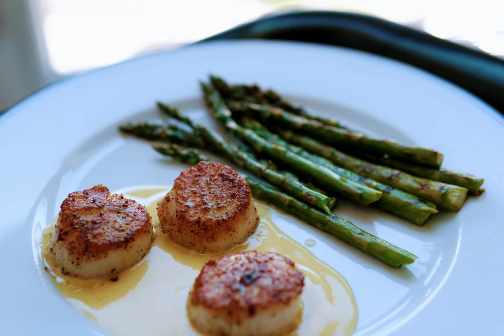 Seared scallops with beurre blanc sauce and grilled asparagus on a white plate.