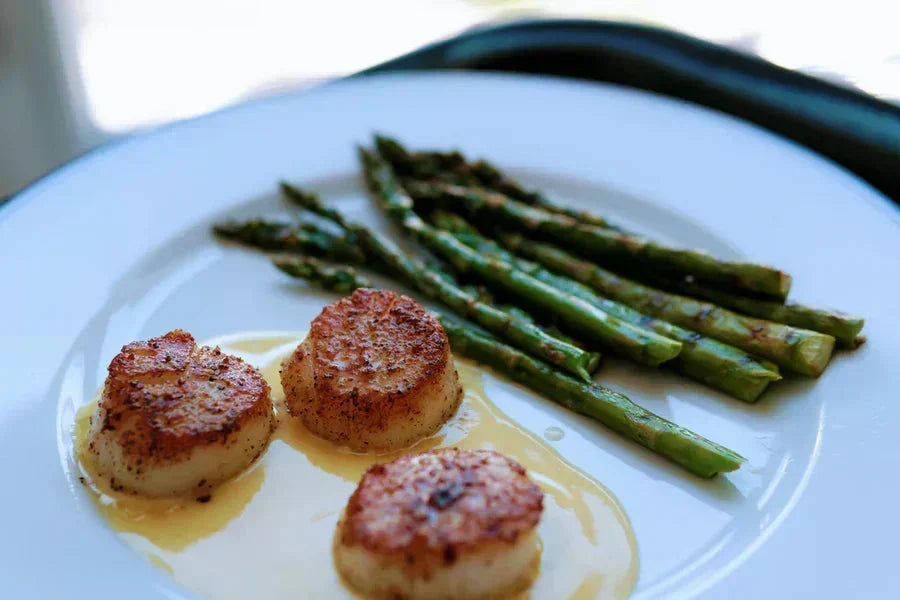 Three seared scallops resting on beurre blanc sauce with a side of grilled asparagus on white plate