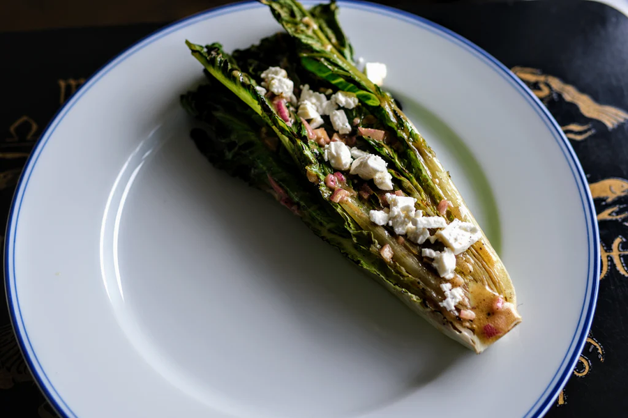 Top-down view of grilled romaine lettuce with charred leaves, crumbled feta and mustard vinaigrette on a white rimmed plate