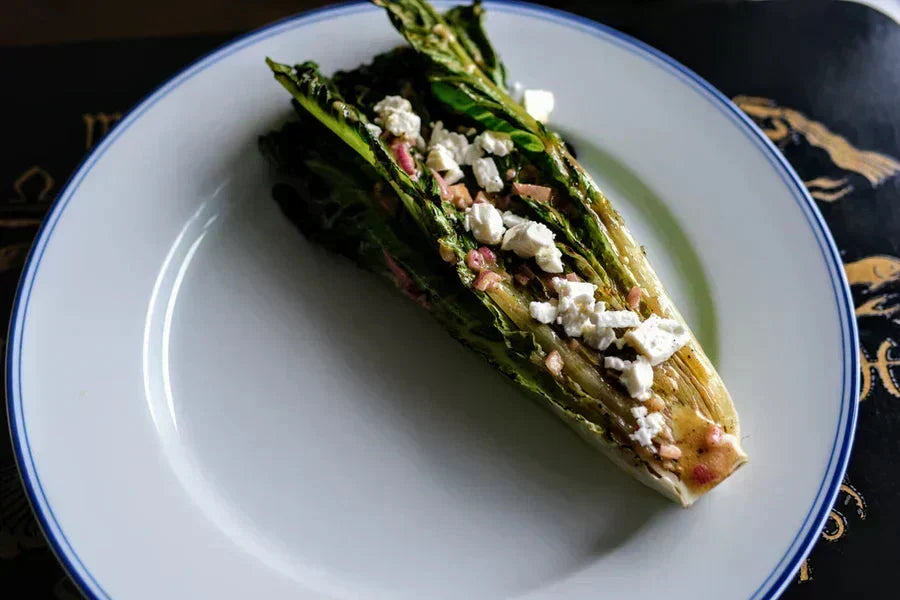 Top-down view of grilled romaine lettuce halves with feta and a shallot-mustard dressing on a plate