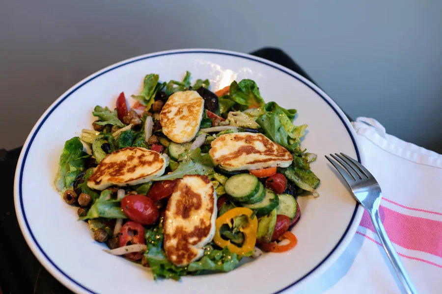 Overhead view of Halloumi salad with fried halloumi, chickpeas, cucumbers, tomatoes on a white plate