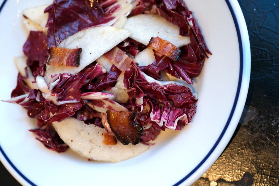 Overhead view of radicchio and Asian pear salad showing pear slices, torn radicchio, and bacon in a white bowl with blue rim