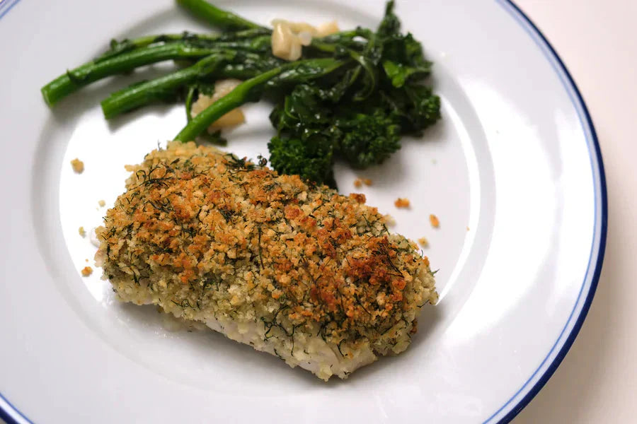 Overhead close-up of panko-crusted cod loin with dill, served with sautéed broccolini on white plate