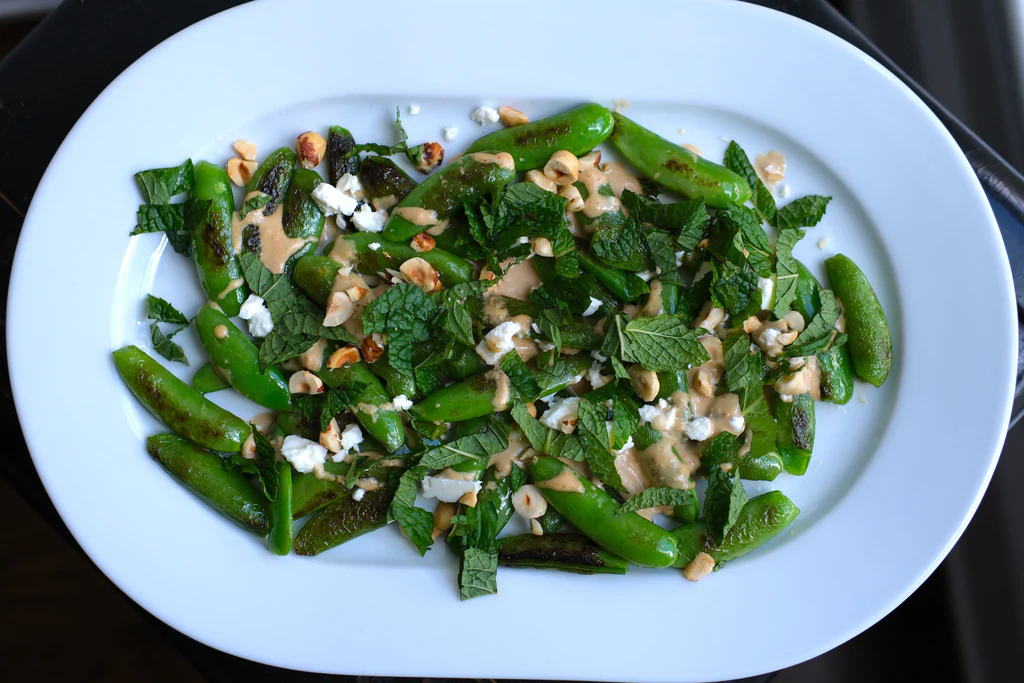 Sugar snap peas with tahini dressing, mint, feta, and toasted hazelnuts on a white oval platter