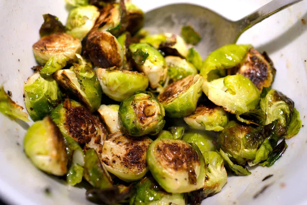 Close-up of roasted halved Brussels sprouts in warm butter-and-vinegar dressing inside a white bowl.