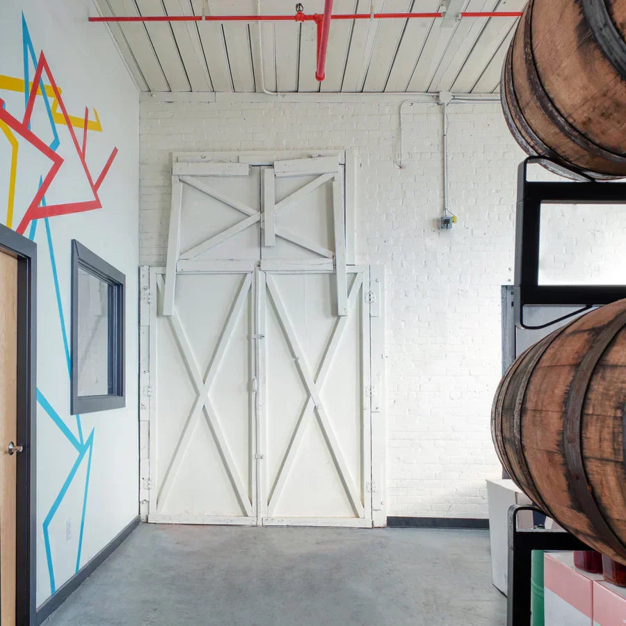 Vinegar workshop interior with stacked wooden barrels, white barn doors, and a colorful mural.