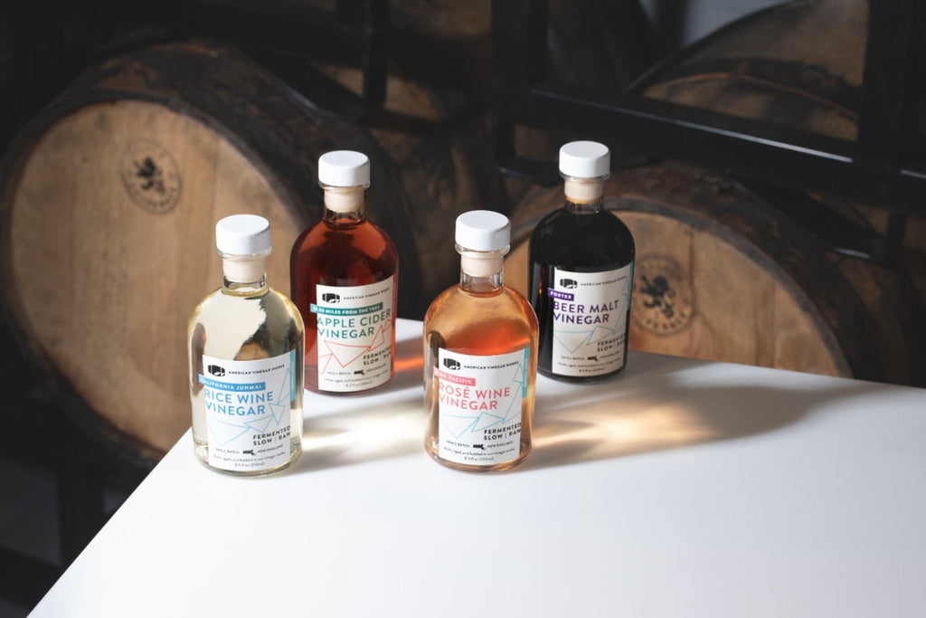 Four small vinegar bottles labeled RICE WINE VINEGAR, APPLE CIDER VINEGAR, ROSÉ WINE VINEGAR and BEER MALT VINEGAR on a white table