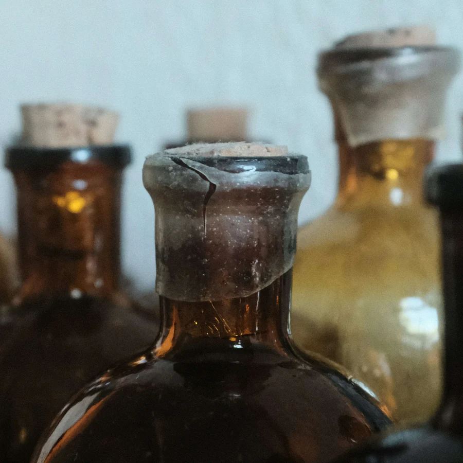 Row of old amber vinegar bottles with corks and wax seals, close-up showing dust and aged glass
