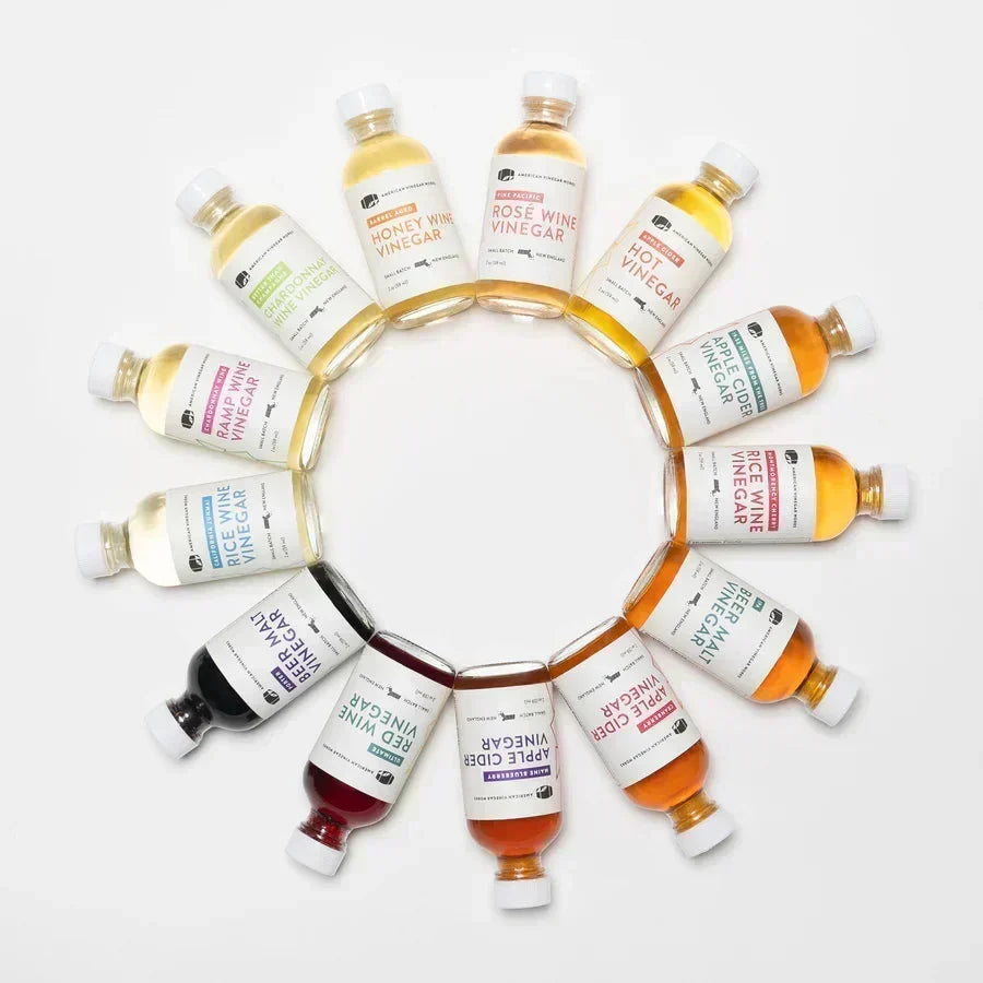 Top-down view of 12 assorted small-batch vinegar bottles arranged in a circle on a white background