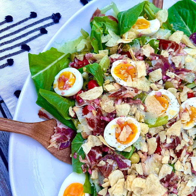 Romaine salad with halved soft‑boiled eggs, shredded cured ham, crushed potato chips and vinaigrette on a white plate