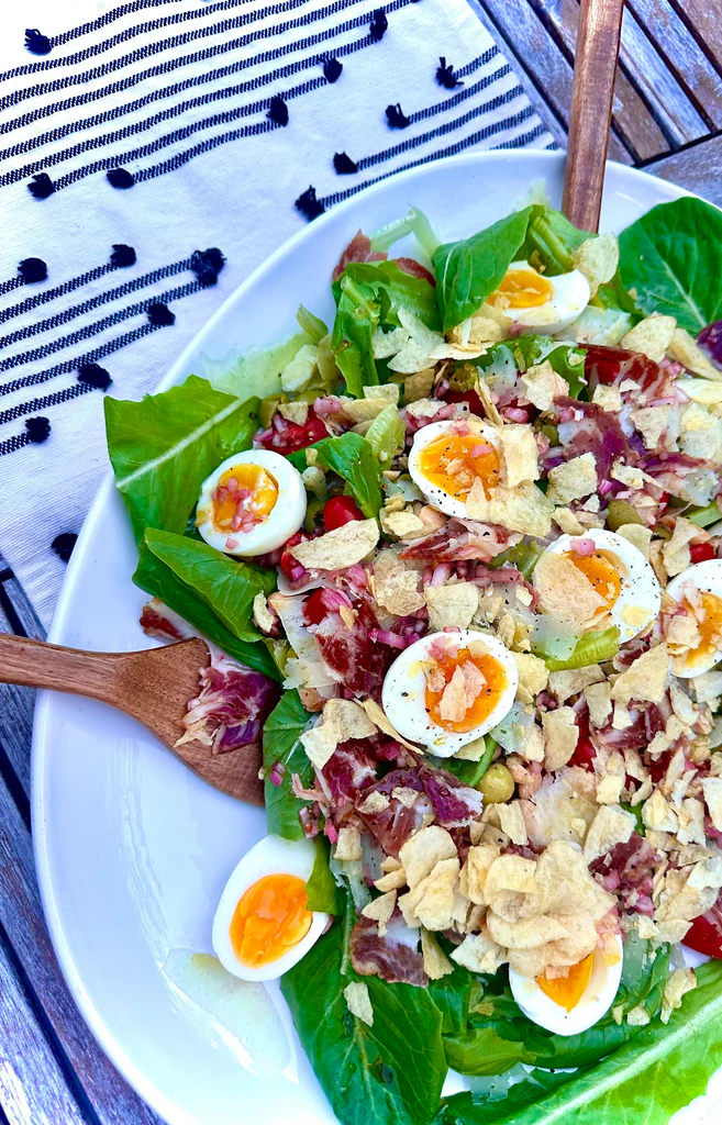 Romaine salad with halved soft‑boiled eggs, shredded cured ham, crushed potato chips and vinaigrette on a white plate