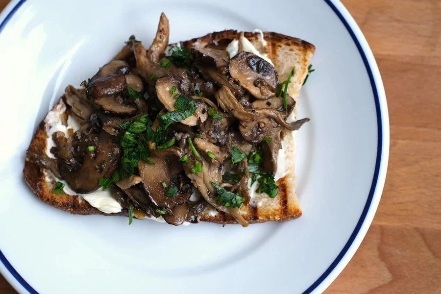 Top-down view of mushroom toast on grilled sourdough showcasing sautéed mushrooms, mascarpone, and chopped parsley on a white plate with blue rim