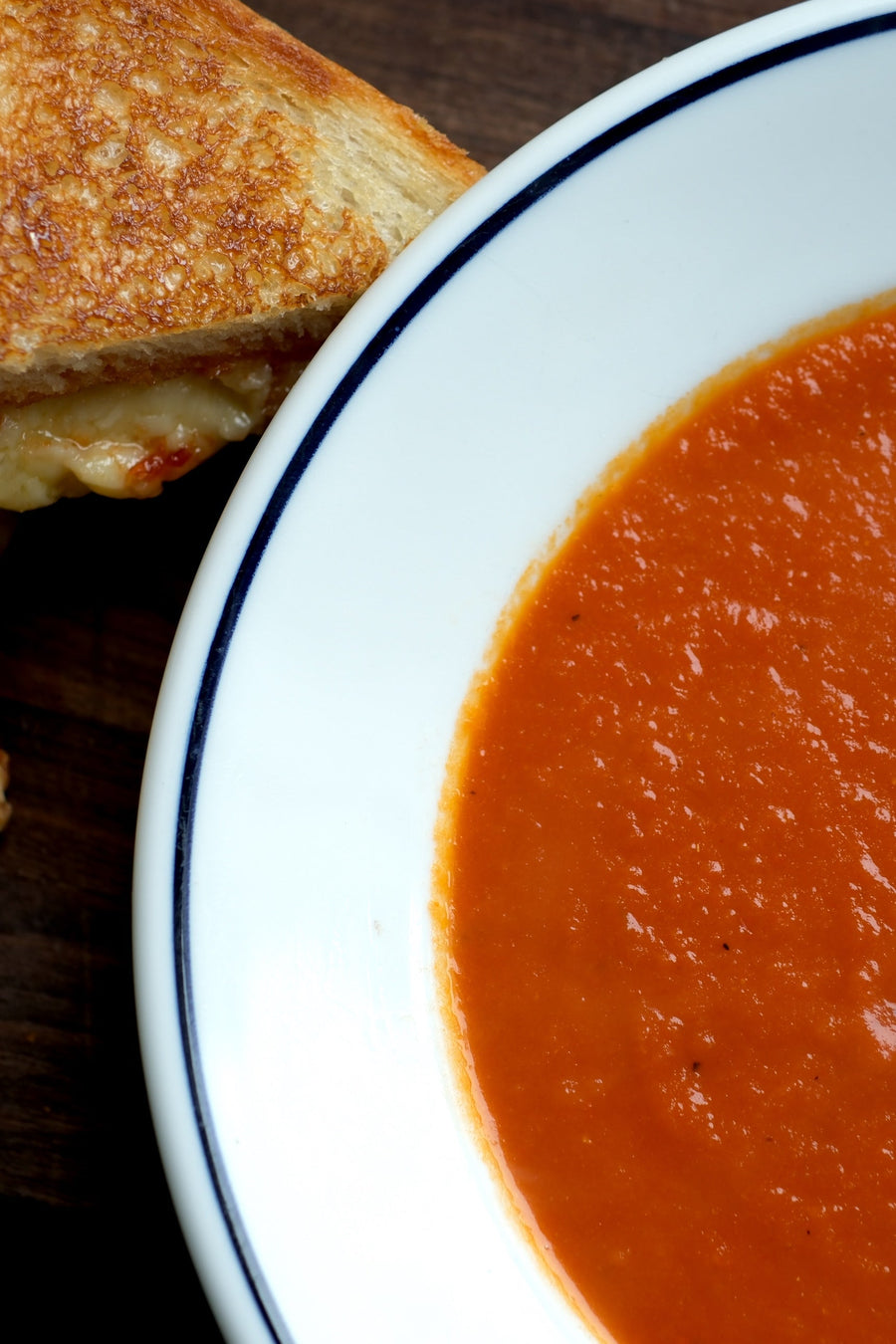 Grilled cheese with spicy pepper jam beside a bowl of tomato soup with chives