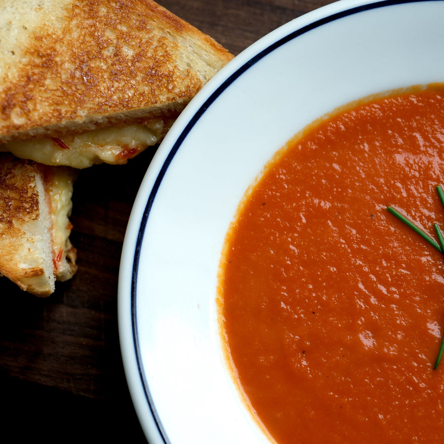 Grilled cheese with spicy pepper jam beside a bowl of tomato soup with chives