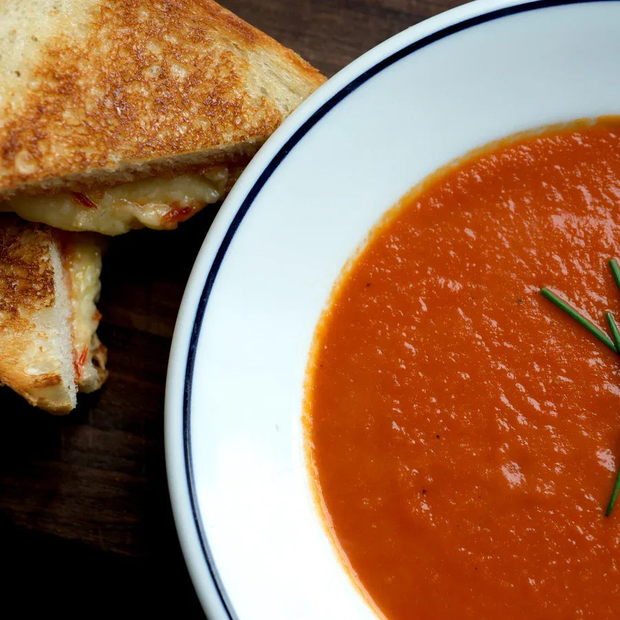 Grilled cheese sandwich with pepper jam served beside a bowl of creamy tomato soup on a dark wooden board
