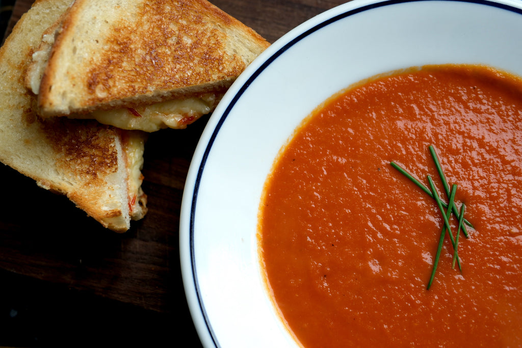 Grilled cheese with spicy pepper jam beside a bowl of tomato soup with chives