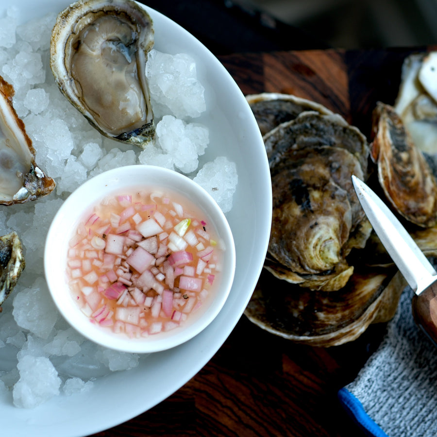 Shucked oysters on ice with mignonette and oyster shucking knife