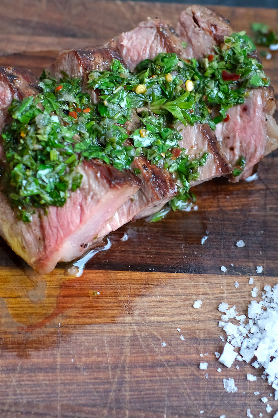 Sliced steak with chimichurri sauce and salt on a wooden cutting board
