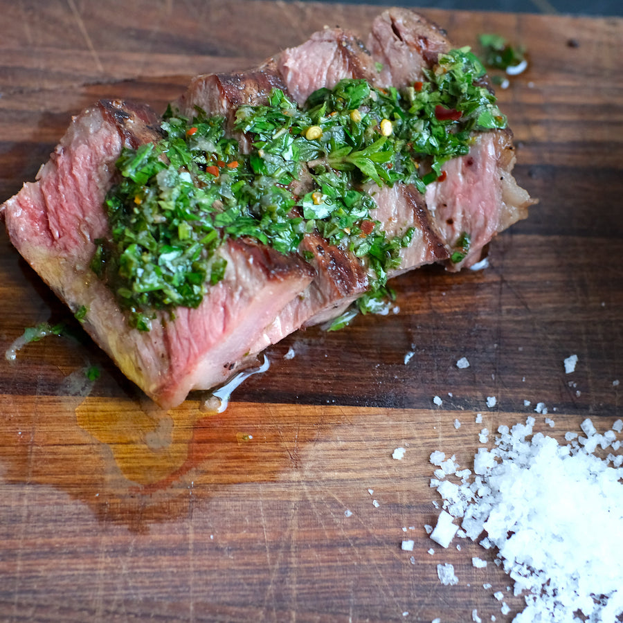 Sliced steak with chimichurri sauce and salt on a wooden cutting board
