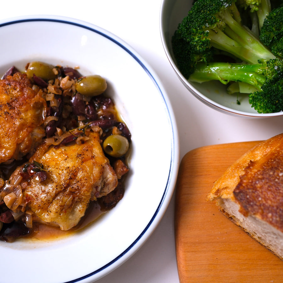 Olive chicken served with steamed broccoli and bread on white plates and cutting board