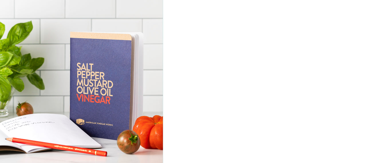 notebooks.  one open one standing. with basil ad tomatoes around them and against a white tile background