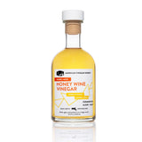 The front view of a 250ml bottle of American Vinegar Works Barrel Aged Honey Wine Vinegar, featuring a white and orange label against a clean white background.