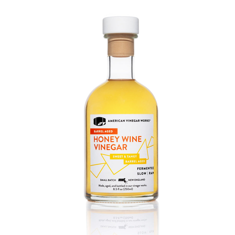 The front view of a 250ml bottle of American Vinegar Works Barrel Aged Honey Wine Vinegar, featuring a white and orange label against a clean white background.