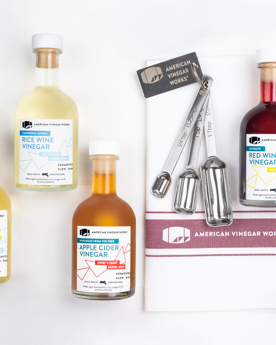 Top-down view of Stocked Kitchen Set with four vinegars and measuring spoons on a white towel.