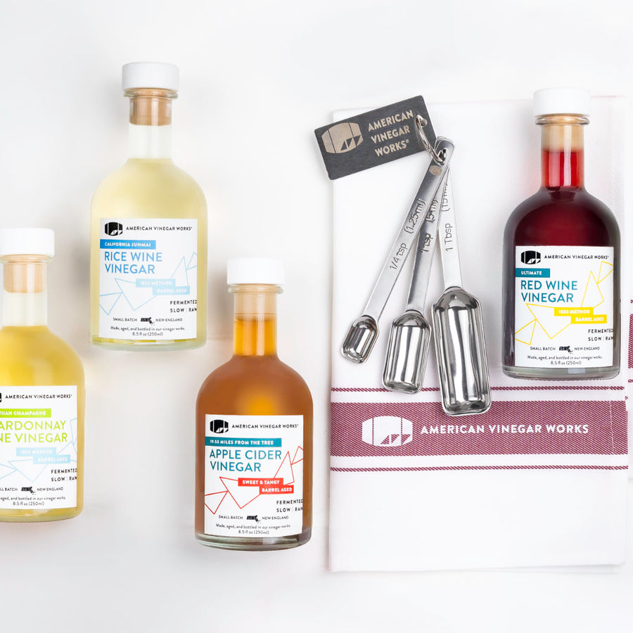 A group photo of four American Vinegar Works vinegar bottles, including Chardonnay, Red Wine, Apple Cider, and Rice Wine vinegars, arranged together on a white background.