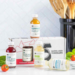Tasting kit with 5 barrel-aged vinegars on a kitchen counter with basil and cherry tomatoes.
