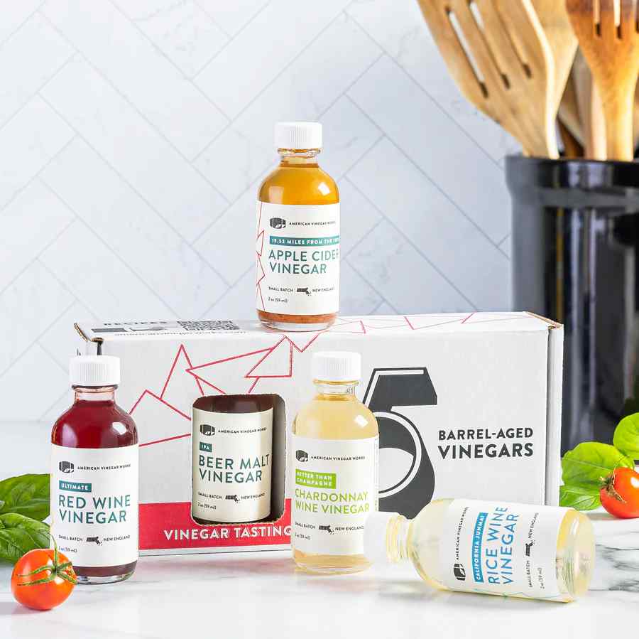 Tasting kit with 5 barrel-aged vinegars on a kitchen counter with basil and cherry tomatoes.