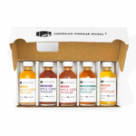 An open box containing five small bottles of American Vinegar Works specialty vinegars.