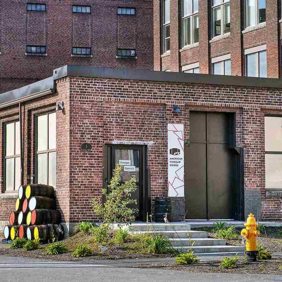 American Vinegar Works brick entrance with 'Vinegar Secrets' door, barrels, and a yellow hydrant.
