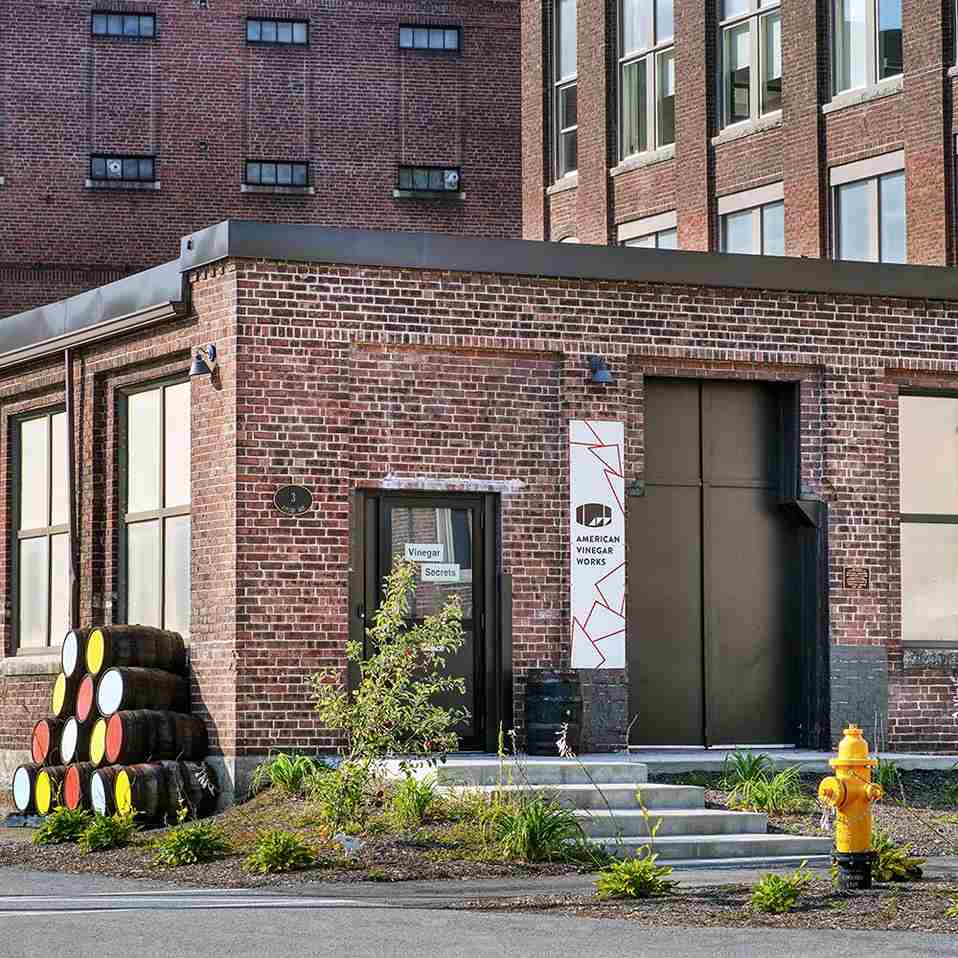 American Vinegar Works brick entrance with 'Vinegar Secrets' door, barrels, and a yellow hydrant.