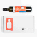 A bottle of American Vinegar Works Extra Virgin Olive Oil lying horizontally above its white product packaging box, which features a red graphic of a bottle and the company logo.