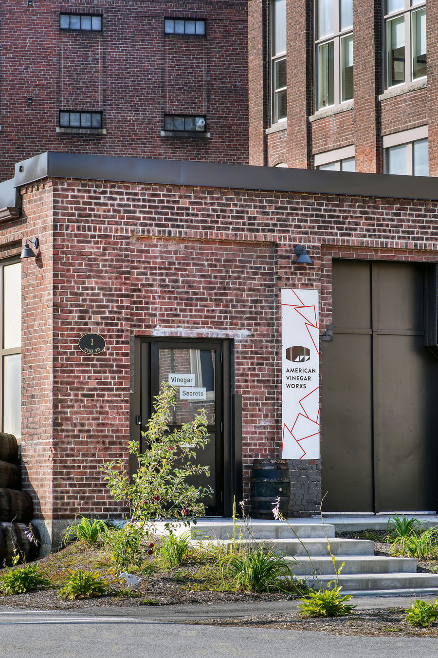 Exterior view of brick American Vinegar Works facility with an entrance sign & stacked wooden barrel