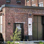 Exterior view of brick American Vinegar Works facility with an entrance sign & stacked wooden barrel