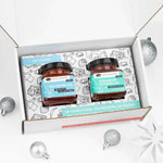 Open white gift box with Red Pepper & Strawberry Rhubarb jam jars, silver ornaments, and snowflakes.