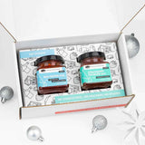 Open white gift box with Red Pepper & Strawberry Rhubarb jam jars, silver ornaments, and snowflakes.