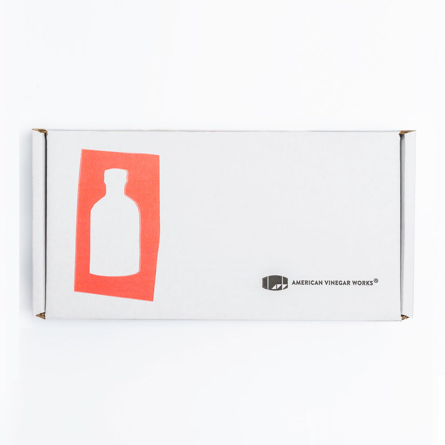 A white American Vinegar Works product packaging box featuring a red graphic of a bottle on the left and the company logo on the bottom right.
